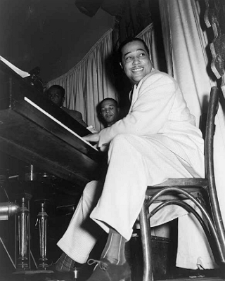 Foto do músico de jazz Duke Ellington sentado numa cadeira e tocando piano