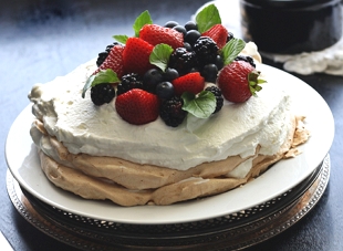 Foto de uma esp&eacute;cie de bolo coberto por um creme branco e com frutas na parte superior.