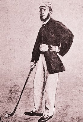 Foto antiga de um homem branco de boné e roupa escura, segurando um taco de golfe