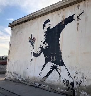 Pintura em parede de rua mostrando um homem vestido de preto atirando um buqu&ecirc; de flores