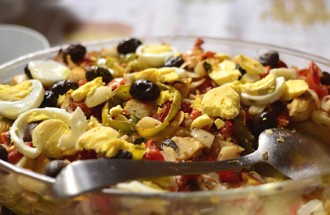 Foto de um prato de bacalhoada com bacalhau, azeitonas pretas, ovo cozido cortado e tomate.