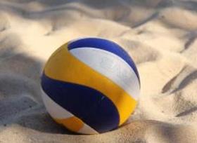 Foto de uma bola de vôlei de praia azul, branca e amarela na areia.