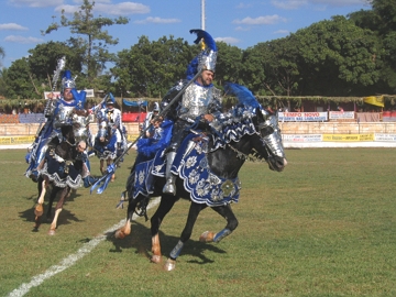 Cavalhada, cavaleiros fantasiados em azul e vermelho montados em cavalos.