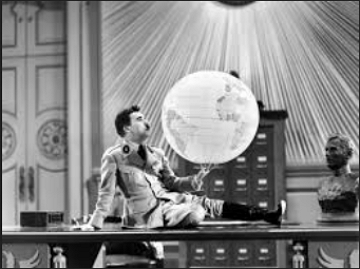 Chaplin com uniforme militar segurando um globo terrestre e sentado numa mesa.
