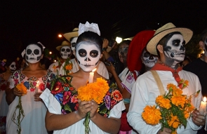 Foto de pessoas com o rosto pintado de caveira e segurando velas e flores