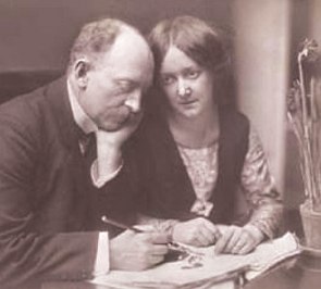 Foto de um homem e uma mulher sentados próximos sendo que o homem está com uma caneta ou lápis na mão