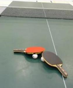 Foto de uma mesa, rede, bolinha e raquetes do tênis de mesa
