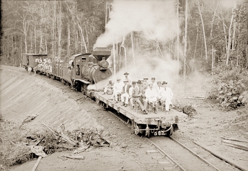 Foto em preto e branco de uma locomotiva soltando fuma&ccedil;a e pessoas na frente dela