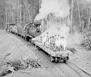 Foto em preto e branco de uma locomotiva soltando fuma&ccedil;a e pessoas na frente dela