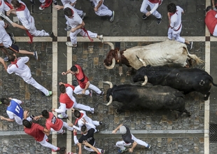 Foto a&eacute;rea de tr&ecirc;s touros correndo atr&aacute;s de pessoas numa rua