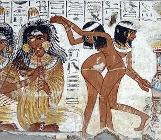 Pintura eg&iacute;pcia mostrando uma mulher tocando uma esp&eacute;cie de flauta e duas eg&iacute;pcias dan&ccedil;ando.
