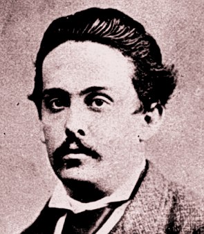 Foto preto e branco, amarelada, de homem branco com cabelo curto e bigode preto, olhando s&eacute;rio.