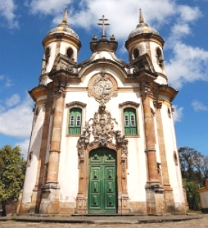 Foto de uma igreja católica pequena com duas torres e portas e janelas verdes