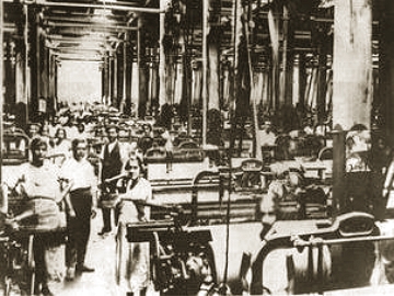 Foto da parte interna de uma ind&uacute;stria antiga do Brasil mostrando as m&aacute;quinas e oper&aacute;rios.