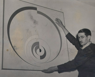 Foto de Ivan Serpa segurando uma obra de arte