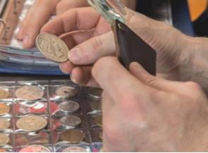 M&atilde;o de um numismata com uma lupa analisando uma moeda antiga