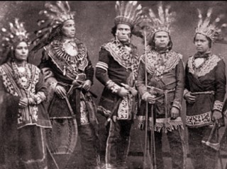 Foto de 5 ind&iacute;genas oj&iacute;buas com roupas t&iacute;picas e cocares na cabe&ccedil;a.