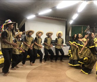 Homens e mulheres dan&ccedil;ando com roupas t&iacute;picas de cor amarelo e preto.